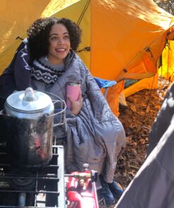 Woman keeping warm with blanket in front of tent.